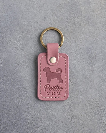 Parisian Blossom rose leather keychain debossed with a Portuguese water dog and the words Portie MOM, on gray concrete