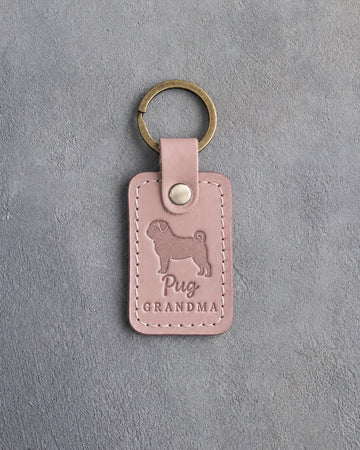 Blush pink leather keychain debossed with a pug silhouette and the words Pug GRANDMA, on gray concrete