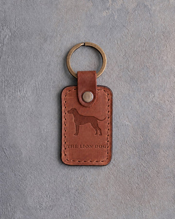 Arizona tan leather keychain debossed with a Rhodesian Ridgeback silhouette above THE LION DOG, on gray concrete