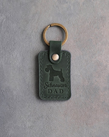 Forest green leather keychain debossed with a Miniature Schnauzer silhouette and the words Schnauzer DAD, on gray concrete
