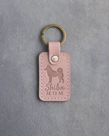 Blush pink leather keychain debossed with a Shiba Inu silhouette and the words Shiba MOM, on gray concrete