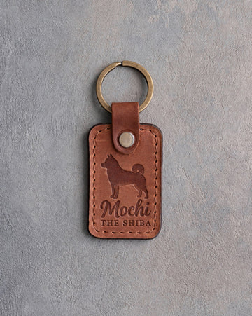Arizona tan leather keychain debossed with a Shiba Inu silhouette, the name Mochi and THE SHIBA, on gray concrete