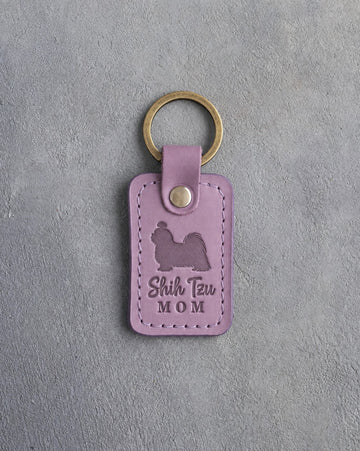 Lilac leather keychain debossed with a Shih Tzu silhouette and the words Shih Tzu MOM, on gray concrete