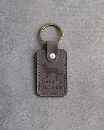 Country gray leather keychain debossed with a border collie and the phrase Smarter THAN ME, on gray concrete