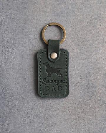 Forest green leather keychain debossed with a springer spaniel silhouette and Springer DAD on gray concrete