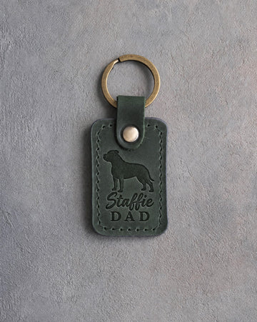 Forest green leather keychain debossed with an American Staffordshire Terrier silhouette and the words Staffie DAD, on gray concrete