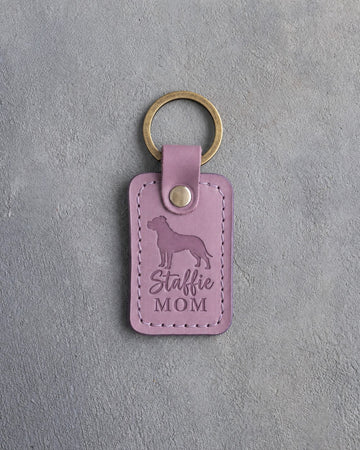 Lilac leather keychain debossed with an American Staffordshire Terrier silhouette and the words Staffie MOM, on gray concrete