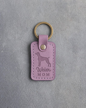 Lilac leather keychain with a debossed weimaraner and the words Weim MOM on gray concrete
