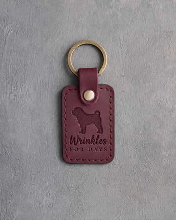 Sangria red leather keychain debossed with a Shar Pei silhouette and the words Wrinkles FOR DAYS, on gray concrete