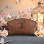 Tan leather makeup pouch debossed with a floral initial, glowing lantern in the background