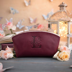 Burgundy leather makeup pouch with a floral initial L and a warm lantern glow behind