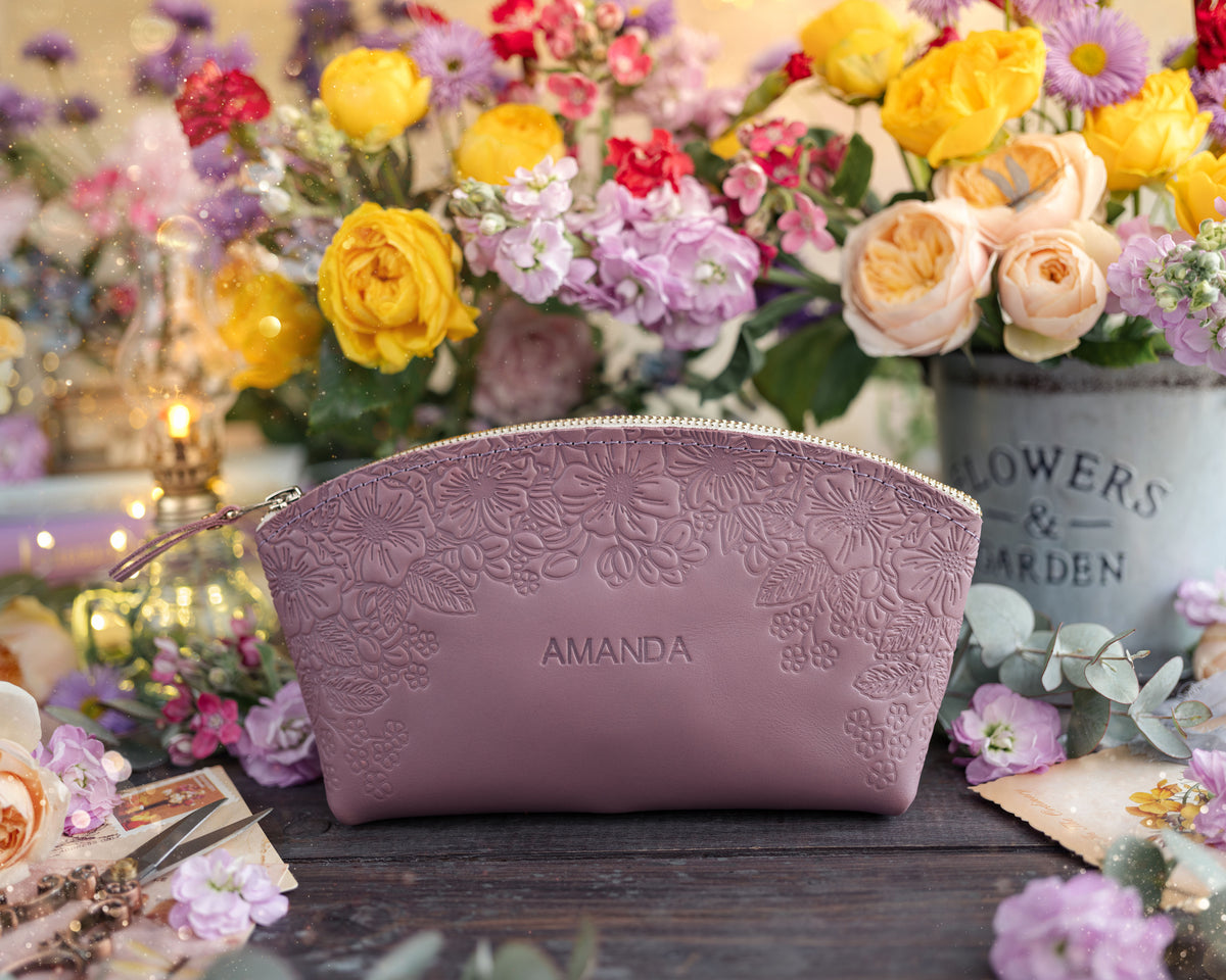 Personalized leather makeup bag with an all-over floral emboss in lilac, name Amanda, set among bright blooms