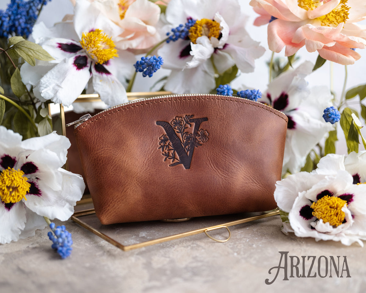 Arizona tan leather makeup pouch with a floral letter V, blue muscari and white flowers around