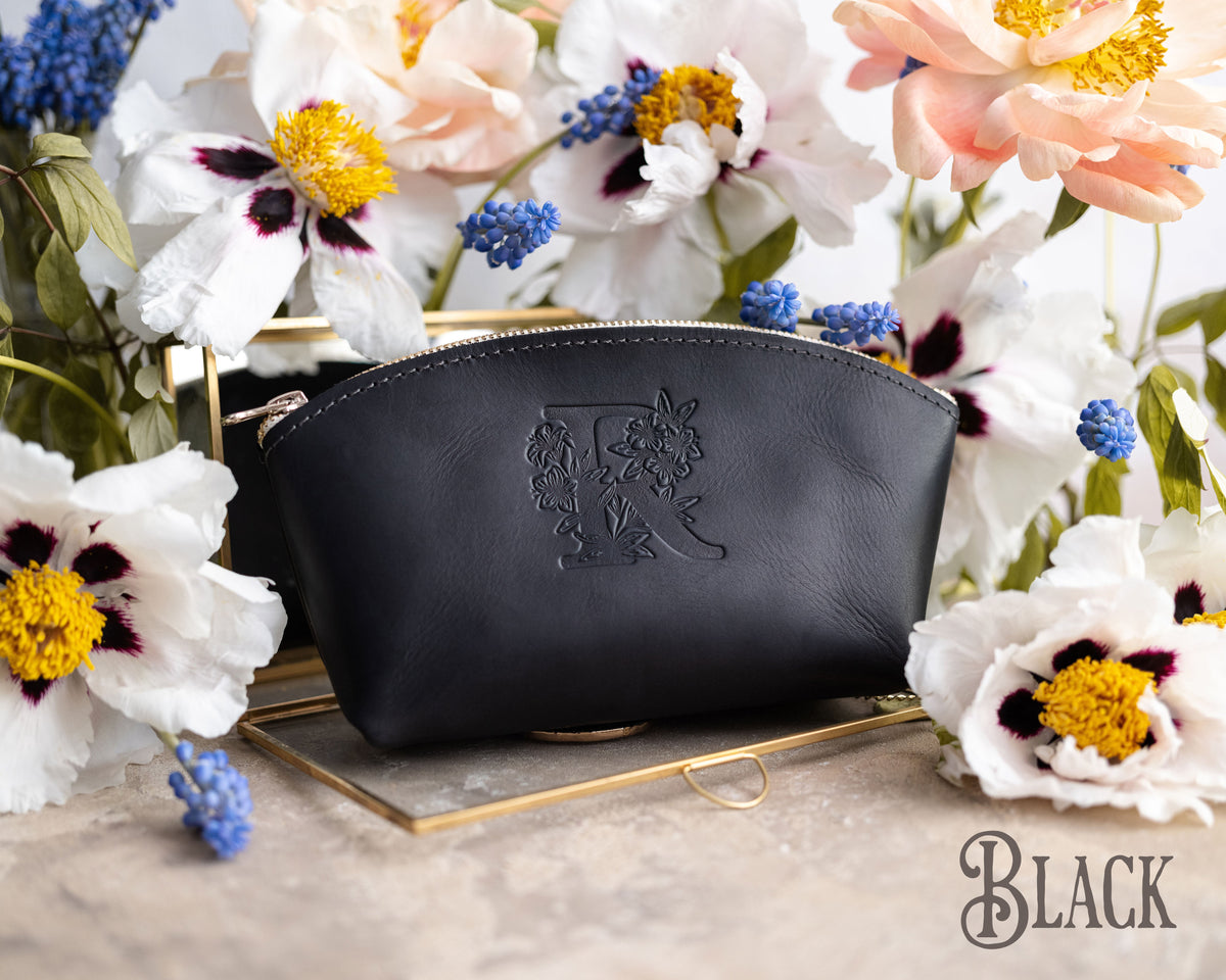 Black leather makeup bag with a floral monogram deboss on a gold tray with spring blooms