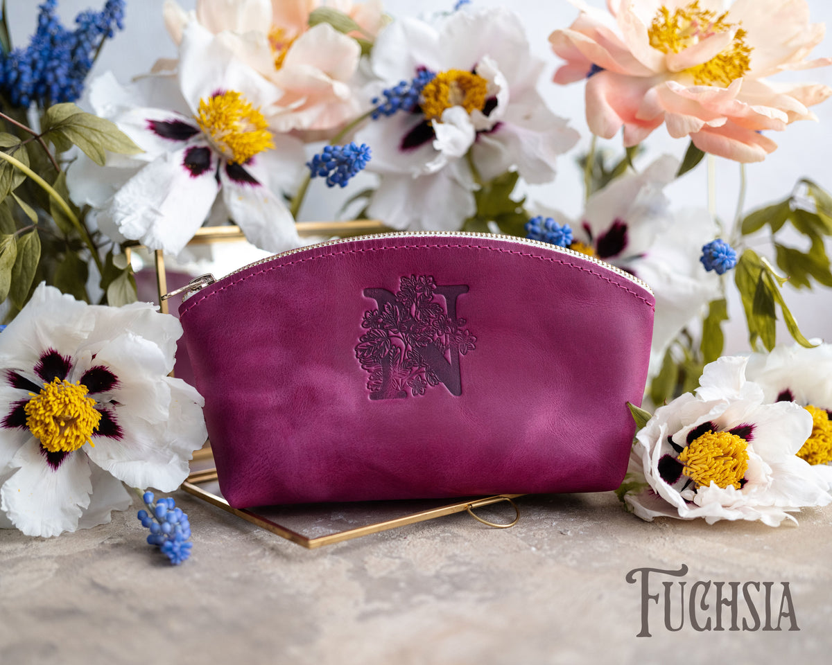 Fuchsia leather makeup pouch with an ornate monogram deboss on a gold tray with blooms