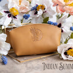 Indian summer golden-tan leather makeup bag with an ornate monogram, white flowers behind