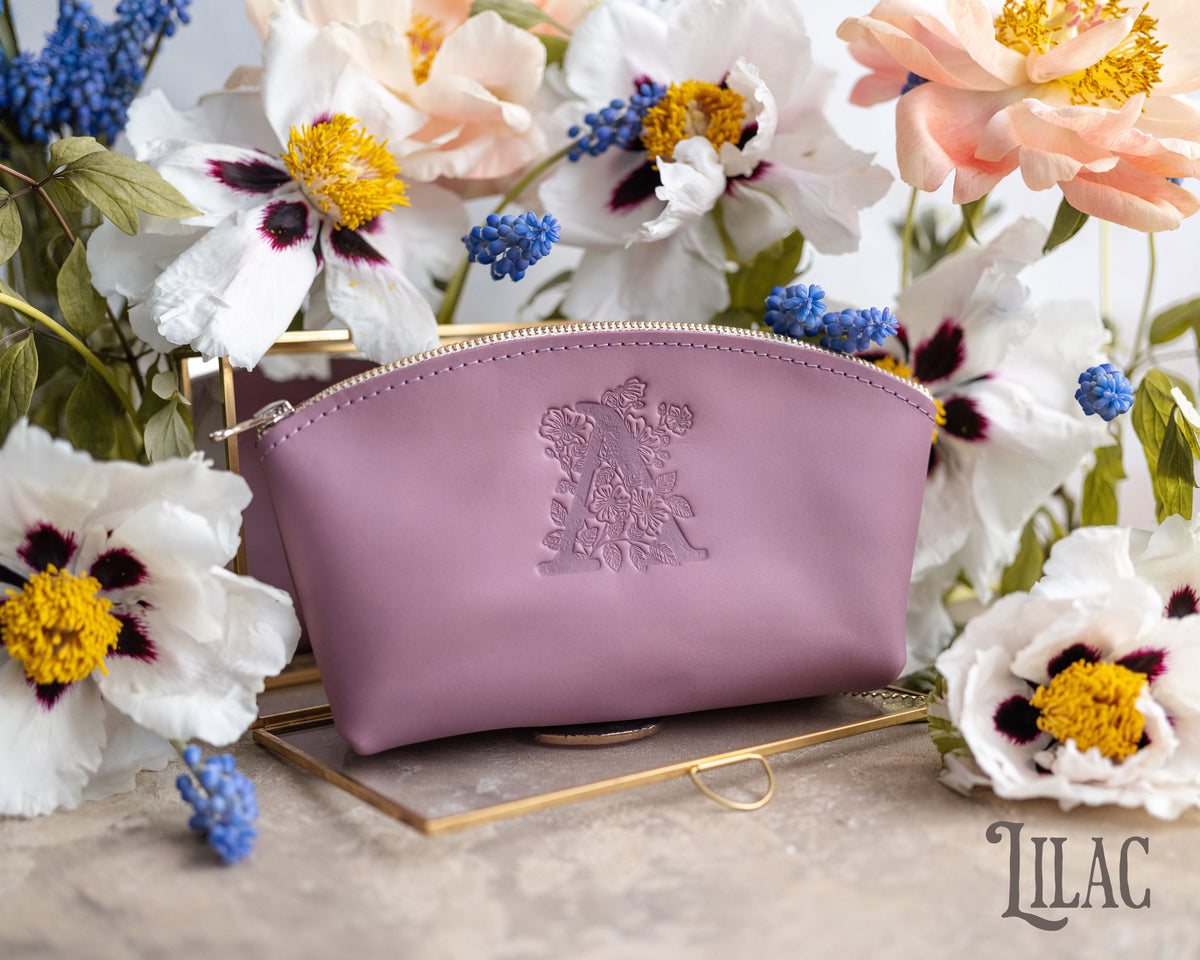 Lilac leather makeup pouch with a floral monogram deboss, styled with fresh blooms