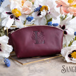 Sangria burgundy leather makeup pouch with a floral initial L, muscari and blooms behind