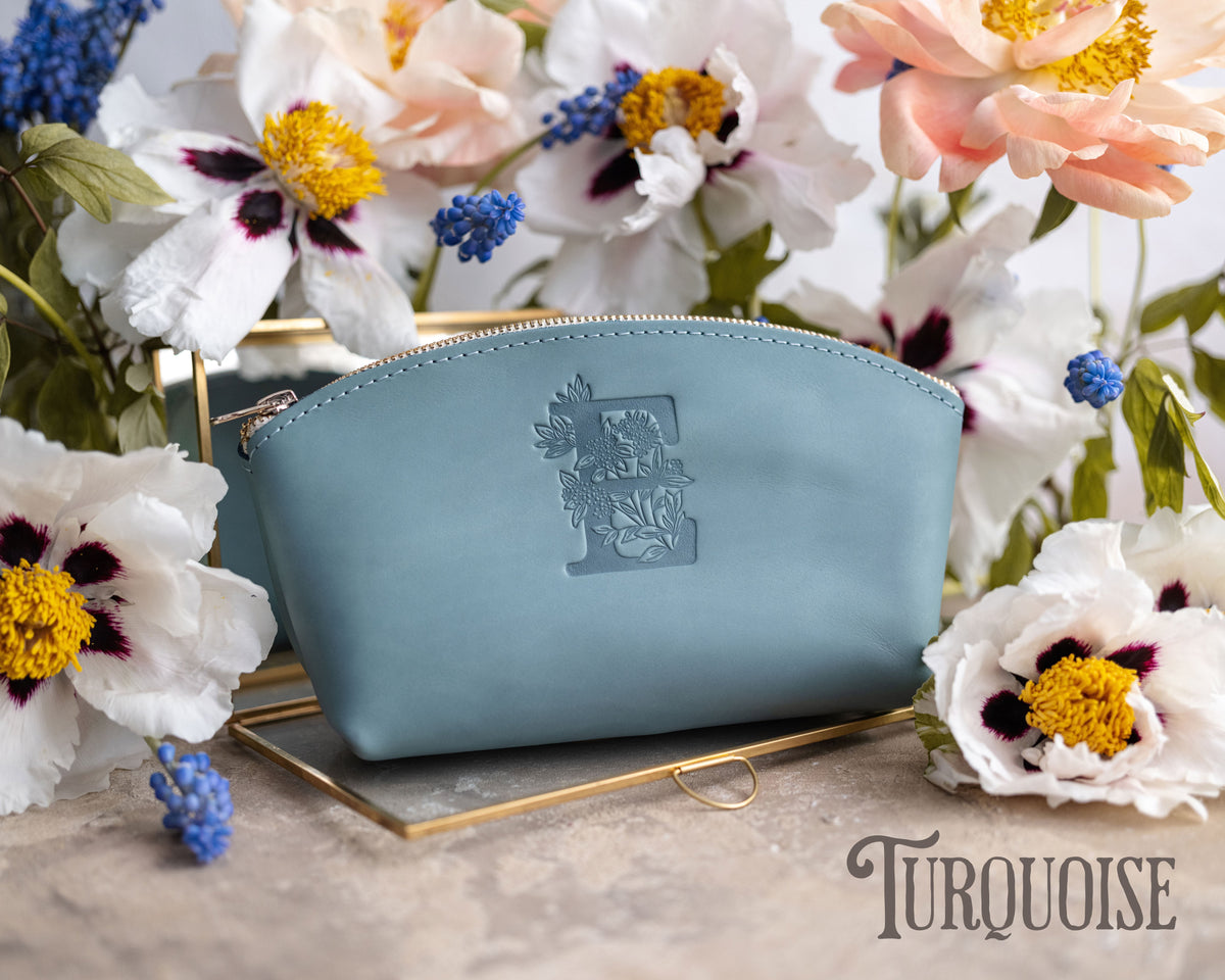 Turquoise pale-blue leather makeup pouch with a floral monogram, white flowers around