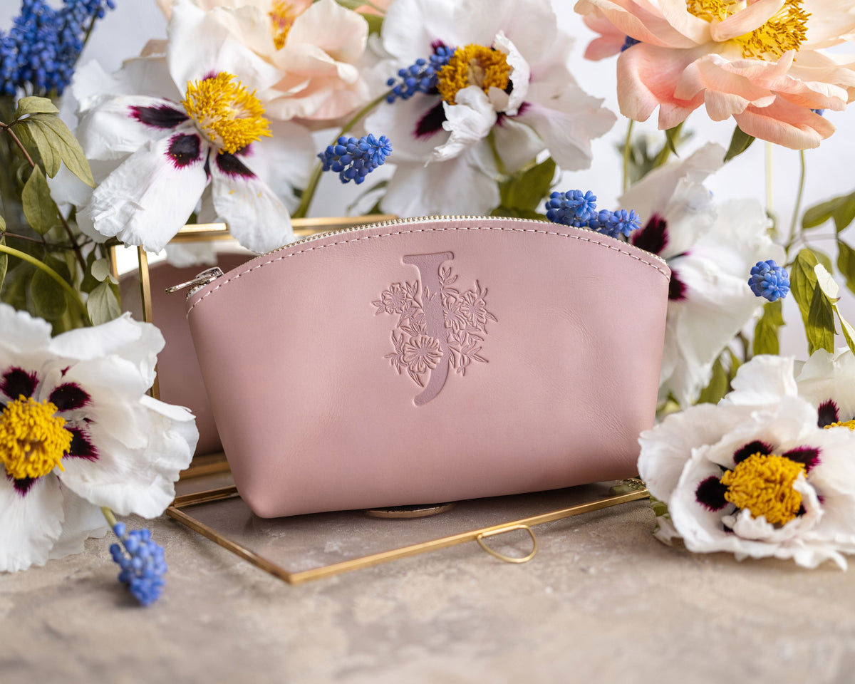 Blush pink leather makeup pouch with a floral letter V, white anemones and muscari behind