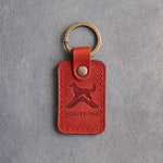 Poppy red leather keychain debossed with a dog on top of an agility A-frame above AGILITY DOG, on gray concrete