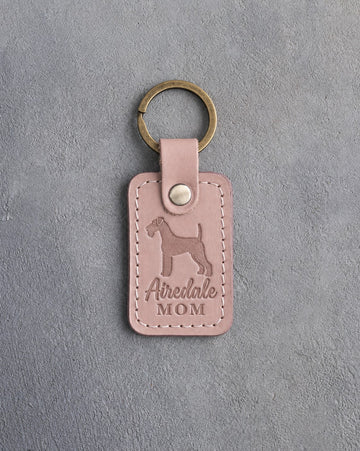 Blush pink leather keychain with a debossed Airedale terrier and the words Airedale MOM, on gray concrete