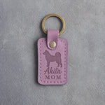Lilac leather keychain with a debossed Akita and the words Akita MOM on gray concrete