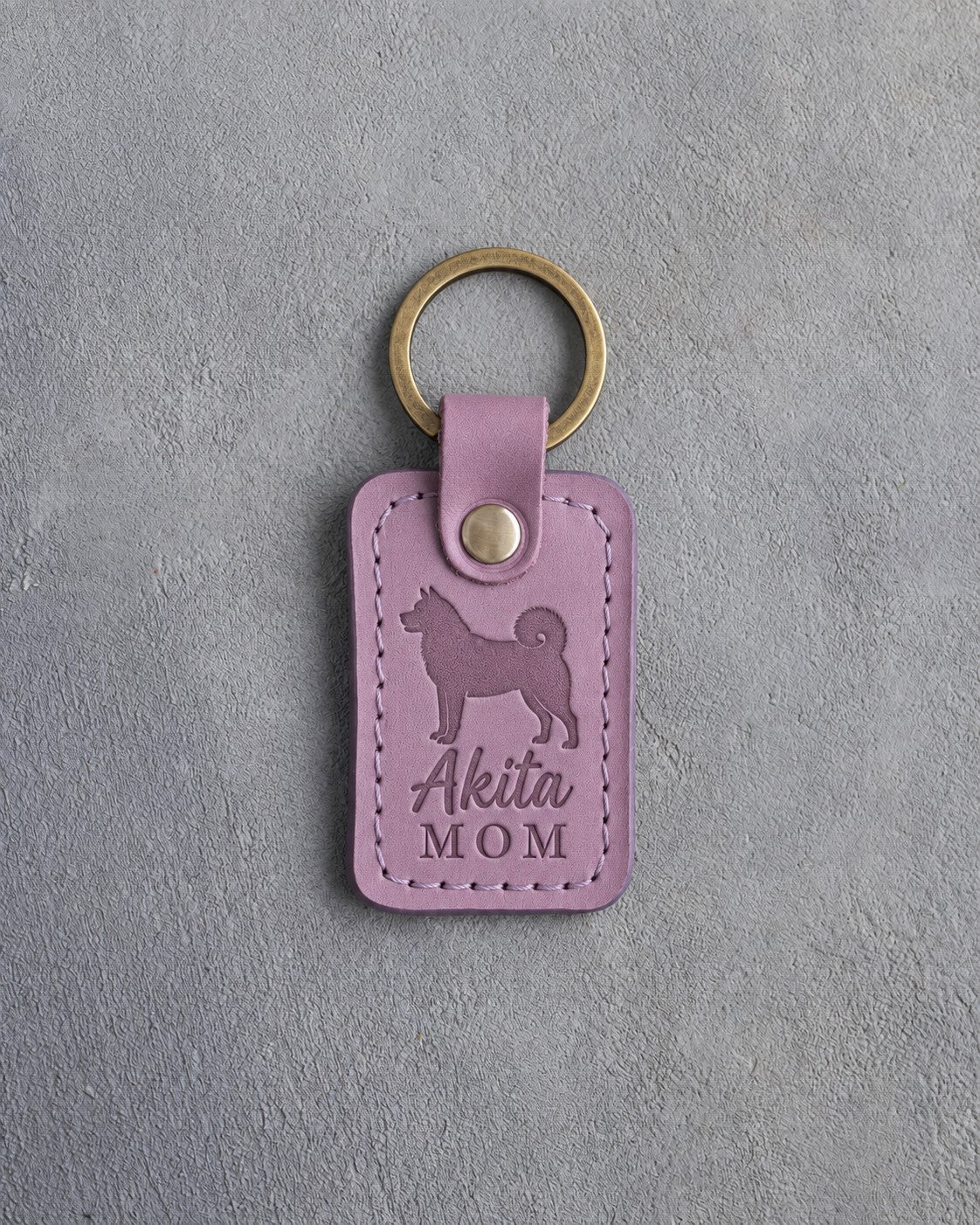 Lilac leather keychain with a debossed Akita and the words Akita MOM on gray concrete