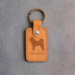 Indian Summer tan leather keychain debossed with an Akita above THE AKITA, on gray concrete