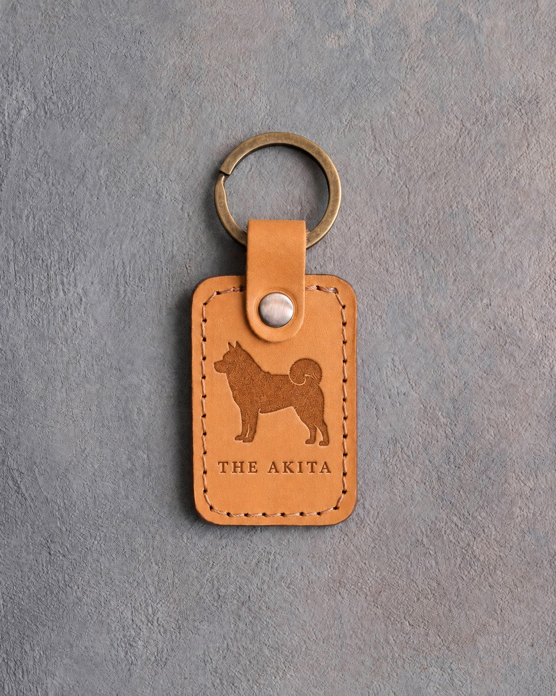 Indian Summer tan leather keychain debossed with an Akita above THE AKITA, on gray concrete