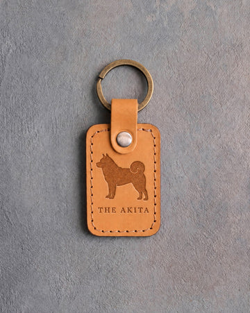 Indian Summer tan leather keychain debossed with an Akita above THE AKITA, on gray concrete