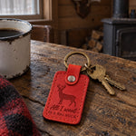 Red All I Want Is a Big Buck keychain peeking from the top of a knit Christmas stocking hung on a log mantel