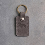 Country gray leather keychain debossed with an American Staffordshire Terrier silhouette above THE STAFFIE, on gray concrete