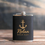 Black leather-wrapped hip flask stamped in gold foil with an admiralty anchor above Nolan and HOLD FAST, on a wooden table