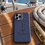 Blueberry Nolan HOLD FAST iPhone case in full-grain leather on the worn teak cockpit table of a sailboat beside a coiled white dock line