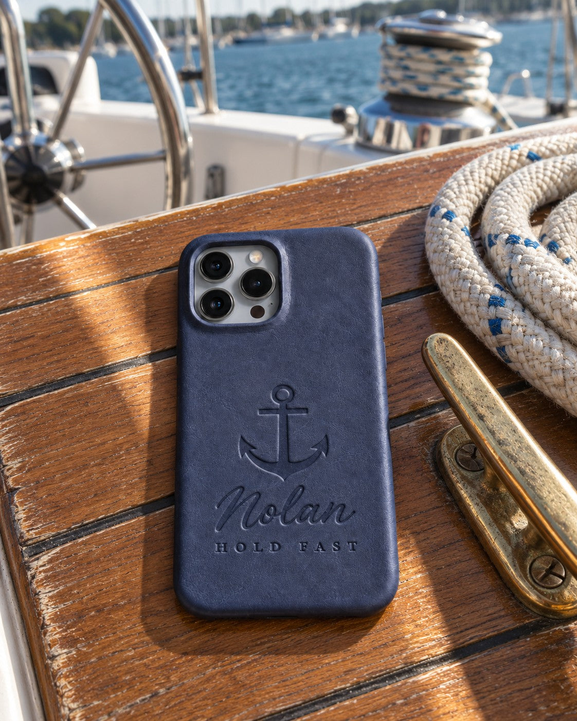 Blueberry Nolan HOLD FAST iPhone case in full-grain leather on the worn teak cockpit table of a sailboat beside a coiled white dock line