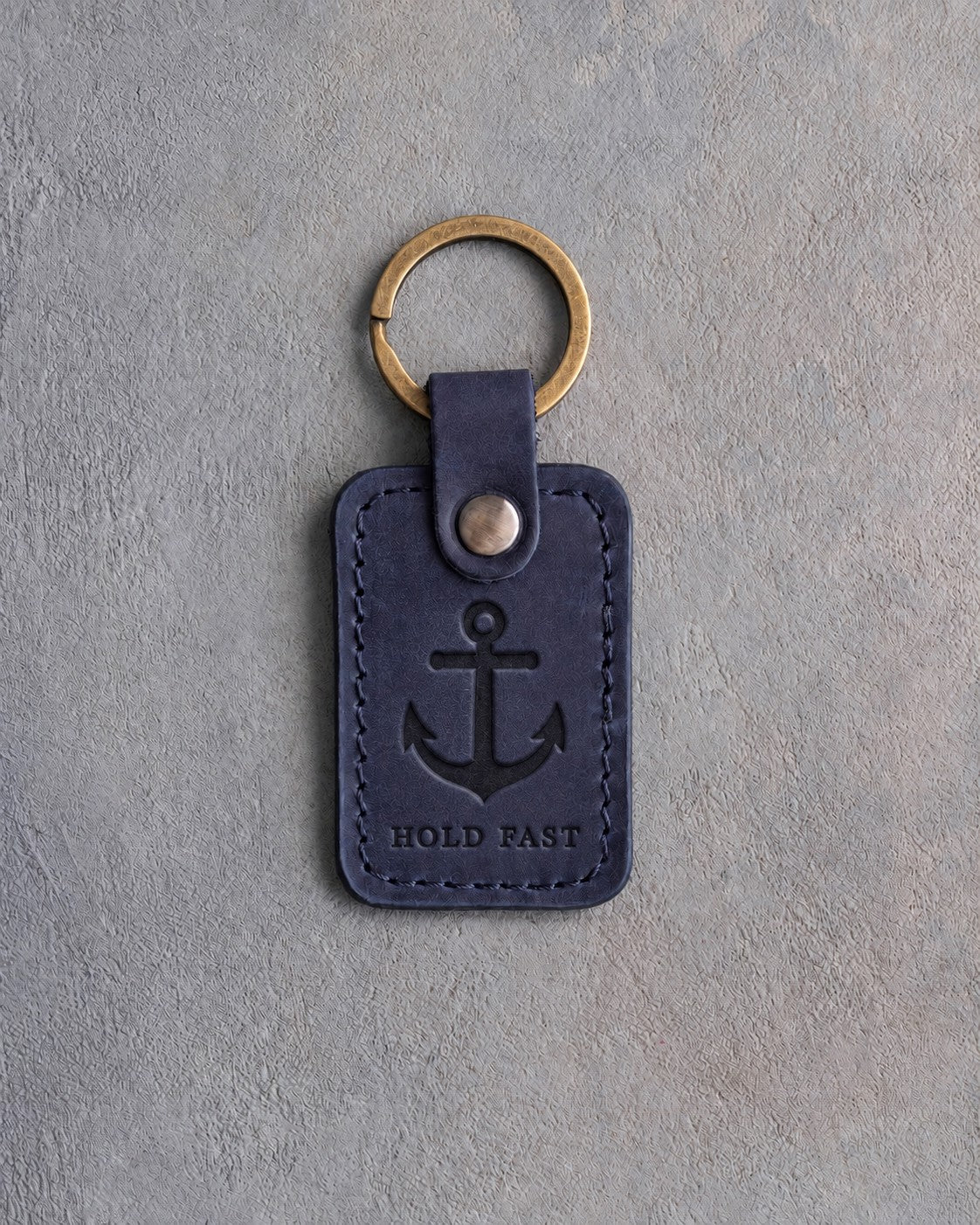 Blueberry leather keychain debossed with an admiralty anchor above HOLD FAST, on gray concrete