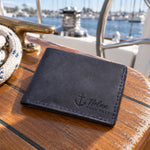 Blueberry Nolan HOLD FAST bifold wallet in full-grain leather on the worn teak cockpit table of a sailboat beside a coiled white dock line