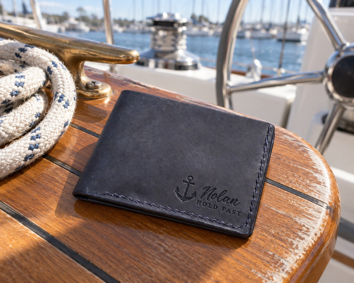 Blueberry Nolan HOLD FAST bifold wallet in full-grain leather on the worn teak cockpit table of a sailboat beside a coiled white dock line