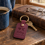 Kelsey SINCE 2019 keychain in sangria leather on a dark oak ranch kitchen table beside a speckled enamel coffee pot