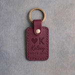 Sangria leather keychain debossed with a Heart K ranch brand above the name Kelsey and SINCE 2019, on gray plaster
