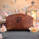 Arizona caramel initial makeup pouch with a floral monogram, staged among pale roses on a slate table