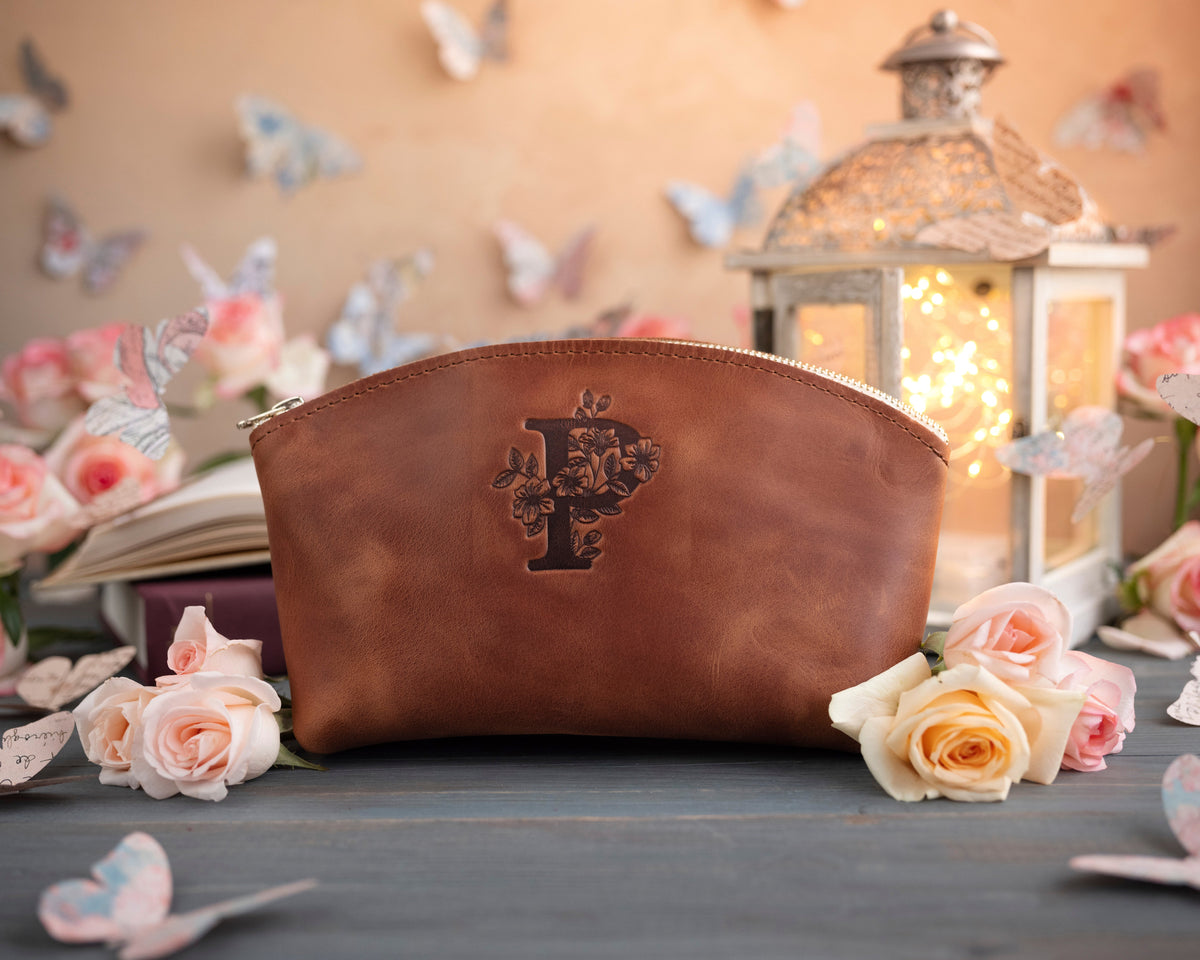 Arizona caramel initial makeup pouch with a floral monogram, staged among pale roses on a slate table