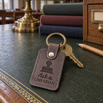 Gray Ask a LIBRARIAN keychain on a library circulation desk beside a returns cart
