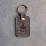 Country gray leather keychain debossed with a library date stamp above Ask a and LIBRARIAN, on gray concrete