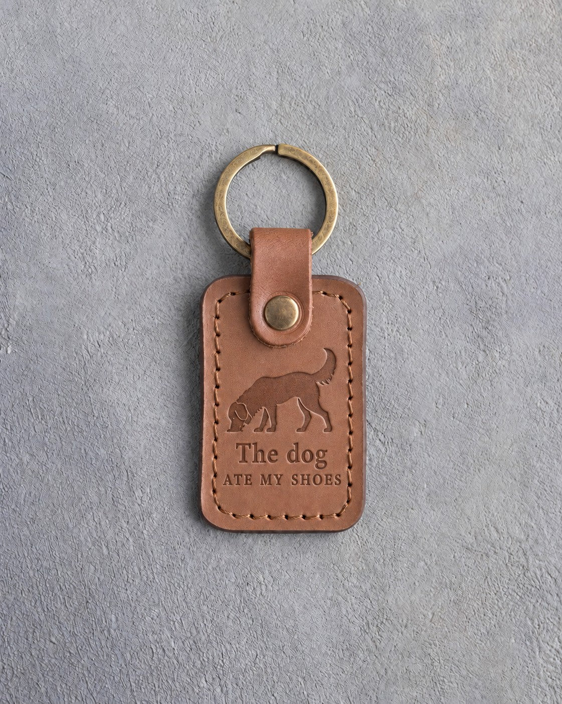 Caramel leather keychain debossed with a dog sniffing the ground above The dog and ATE MY SHOES, on gray concrete
