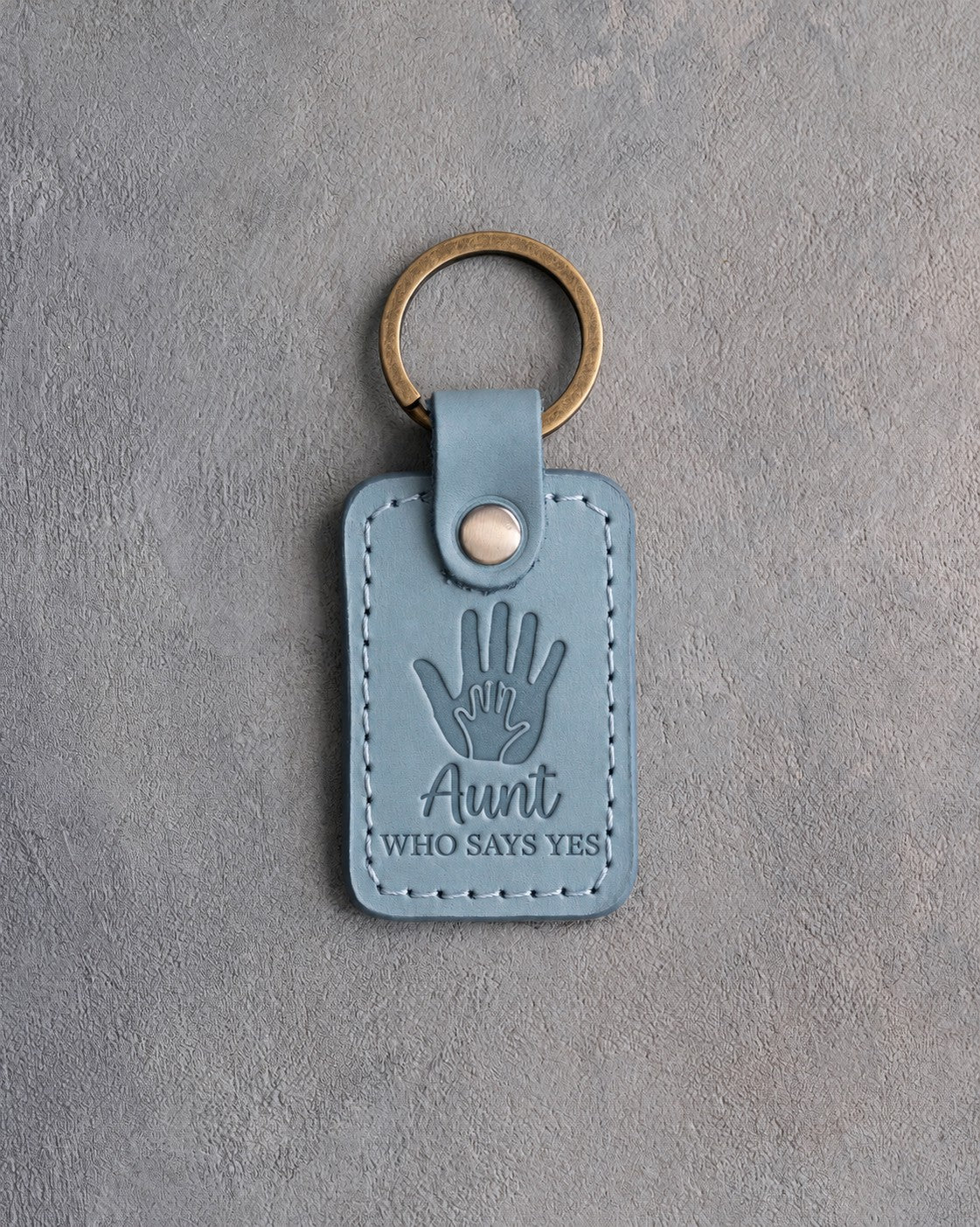 Turquoise leather keychain debossed with a small hand inside a large hand above Aunt and WHO SAYS YES