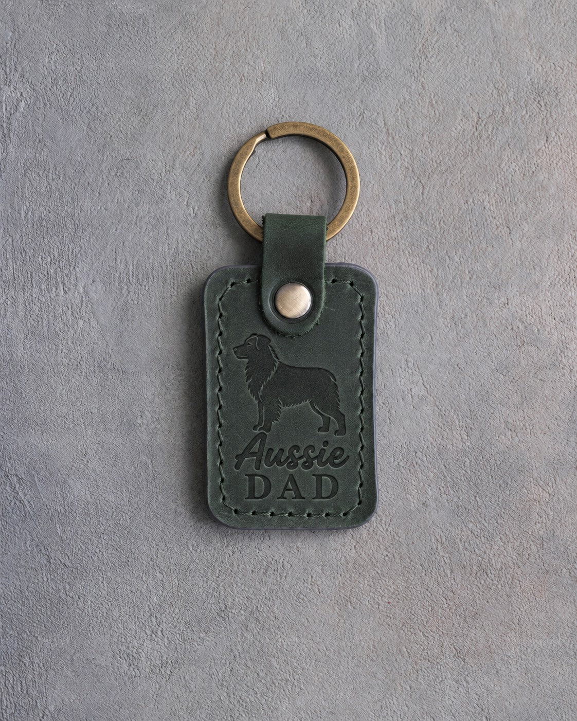 Forest green leather keychain debossed with a Australian Shepherd silhouette and the words Aussie DAD, on gray concrete