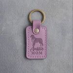Lilac leather keychain debossed with a Australian Shepherd silhouette and the words Aussie MOM, on gray concrete
