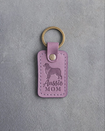 Lilac leather keychain debossed with a Australian Shepherd silhouette and the words Aussie MOM, on gray concrete